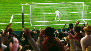 Image of soccer pitch with fans in main focus and goalie and post in foreground.