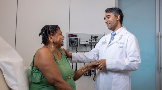 Doctor in white coat holding hands with a seated patient during a consultation in a medical office.