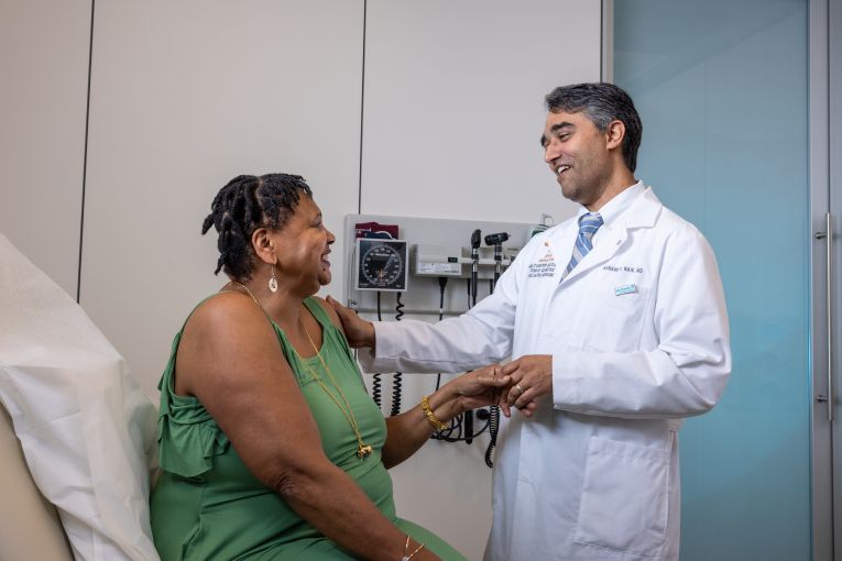 Doctor in white coat holding hands with a seated patient during a consultation in a medical office.
