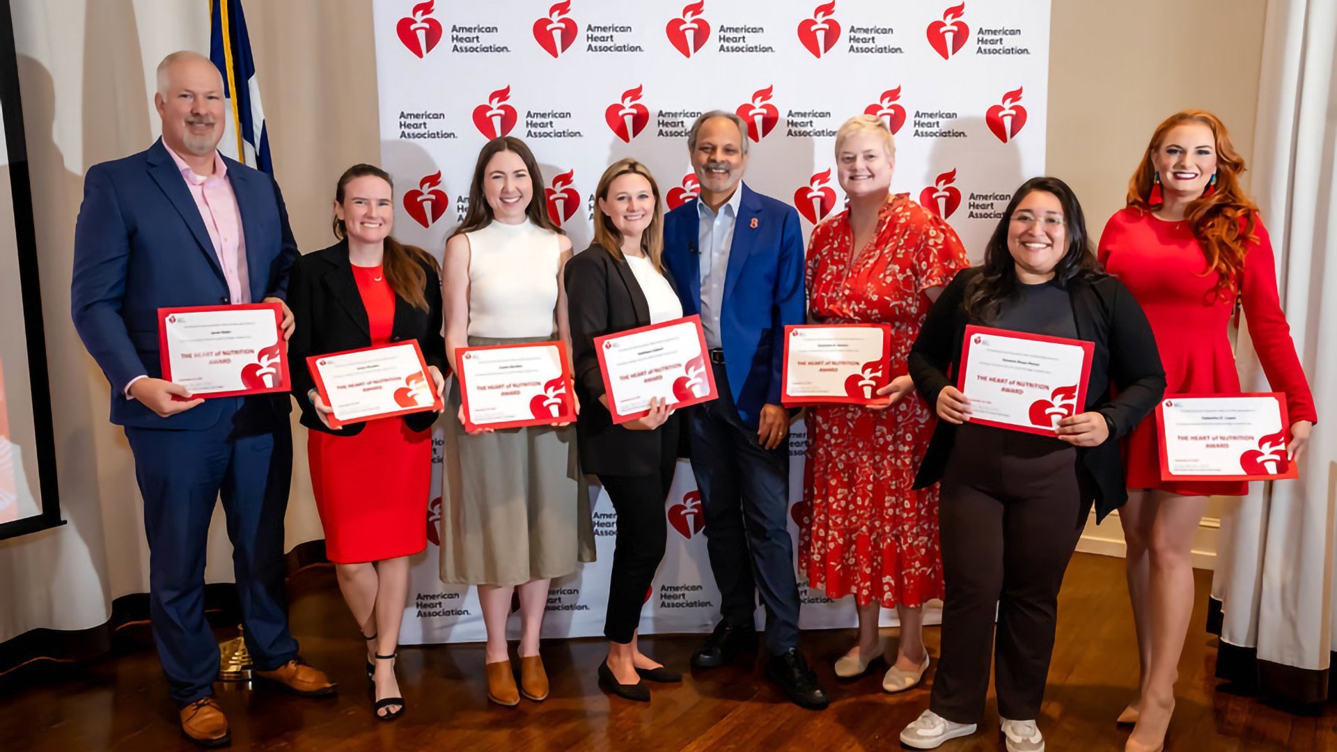 Eight adults posing for a photo holding certificates in front of an American Heart Association backdrop.