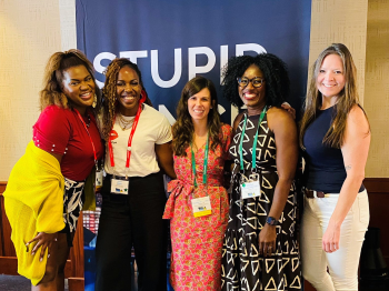 Five women posing together at a meeting.